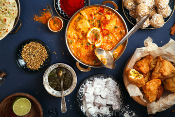 Indian cuisine on diwali holiday: tikka masala, samosa, patties and sweets with mint chutney and spices. Dark blue background, top view.