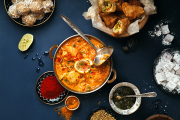 Indian cuisine on diwali holiday: tikka masala, samosa, patties and sweets with mint chutney and spices. Dark blue background, top view.