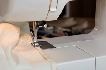The sewing machine's foot with a needle sews ecru color  fabric. Sewing machine details