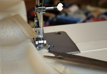 The sewing machine's foot with a needle sews ecru color  fabric. Sewing machine details