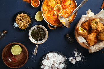 Indian cuisine on diwali holiday: tikka masala, samosa, patties and sweets with mint chutney and spices. Dark blue background, top view.