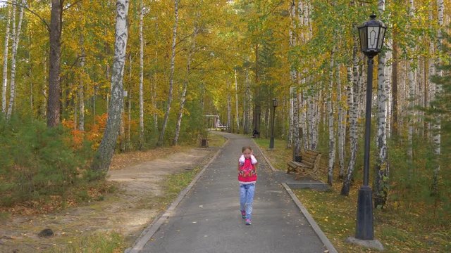 Young girl plugged her ears with her hands and walked along the yellow avenue in the autumn park.