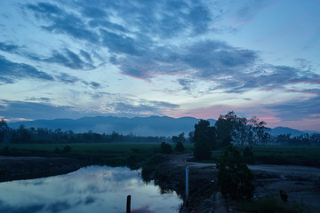 countryside field, soil, forest, pond with twilight sky and clouds reflection on water nearly the mountain at morning before sunrise.