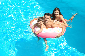 Young couple and cute son with inflatable ring in pool