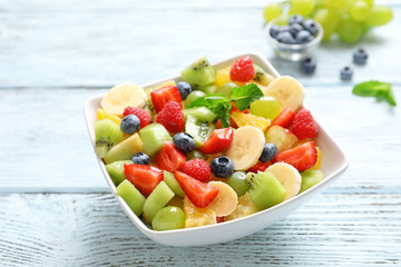 Bowl with yummy fruit salad on wooden table