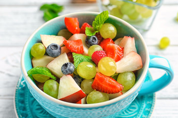 Cup with delicious fruit salad on wooden table