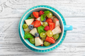 Cup with delicious fruit salad on wooden table