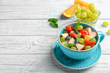 Cup with delicious fruit salad on wooden table