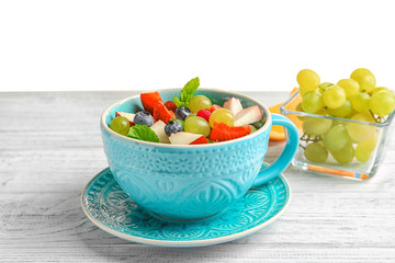 Cup with delicious fruit salad on wooden table