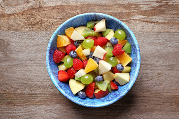 Bowl with yummy fruit salad on wooden table