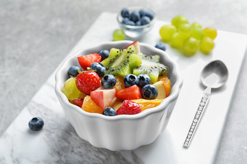 Bowl with yummy fruit salad on marble board