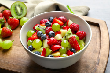 Bowl with yummy fruit salad on wooden board
