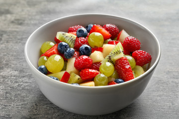 Bowl with yummy fruit salad on grunge table