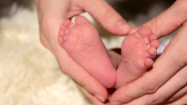 Baby feet in mother hands. Tiny Newborn Baby's feet on female Heart Shaped hands closeup. Mom and her Child. Happy Family concept. Beautiful conceptual video of Maternity.