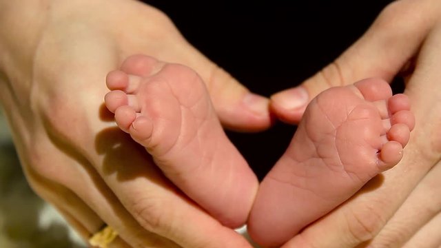 Baby feet in mother hands. Tiny Newborn Baby's feet on female Heart Shaped hands closeup. Mom and her Child. Happy Family concept. Beautiful conceptual video of Maternity.