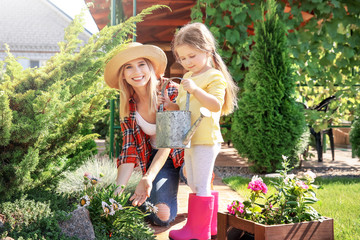 Cute little girl with mother taking care of plants in garden on sunny day