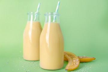 Two bottles with tasty banana smoothie on color background