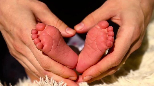 Baby feet in mother hands. Tiny Newborn Baby's feet on female Heart Shaped hands closeup. Mom and her Child. Happy Family concept. Beautiful conceptual video of Maternity.