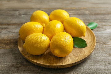 Plate with fresh lemons and leaves on wooden table