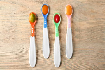 Plastic spoons with baby food on wooden background