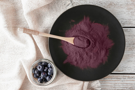 Black plate with acai powder and spoon on wooden background