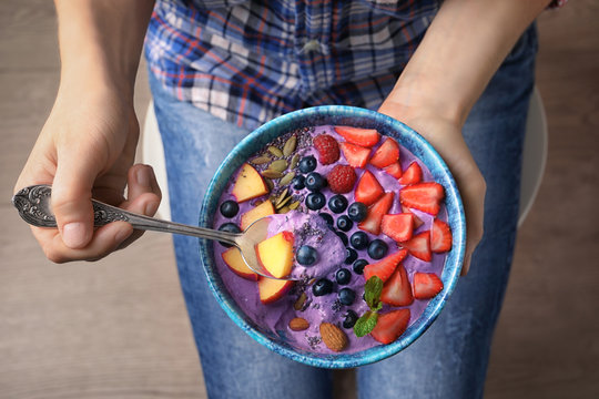 Woman holding spoon and bowl with delicious acai smoothie for healthy breakfast, close up