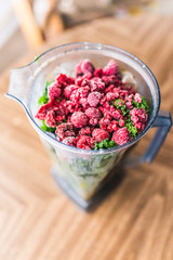 Macro closeup of fresh green kale and frozen raspberries in plastic blender container for smoothie