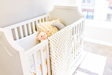 Fototapeta na wymiar Closeup of bright yellow baby crib in nursery room with toys and pillow in model staging home, apartment or house
