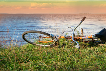 Fototapeta na wymiar The bike lies on the shore. Horizontally.Toned.Orange bicycle on green grass against the background of the river