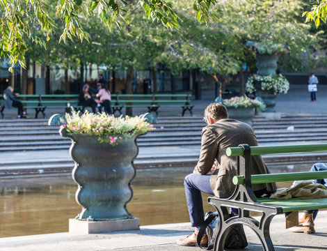 En man njuter av solen vid dammen i  Kungstr&auml;dg&aring;rden med sina m&aring;nga blomster arangemang