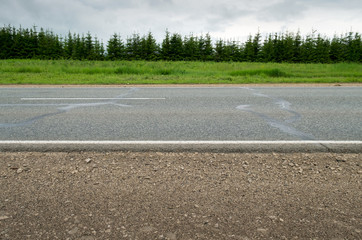 Highway.
Horizontal frame. Asphalt road with white marking is seen from the side, surrounded by green fields and forest
