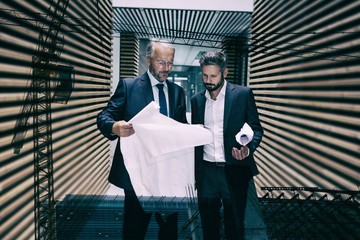 Composite image of businessmen holding plans against crane 