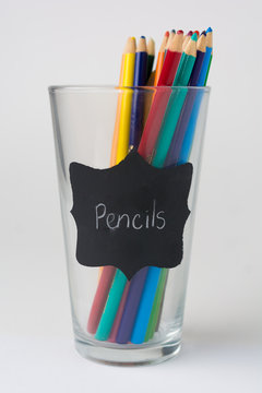Glass Cup of  Pencil Crayons with Chalk Labels on White Background