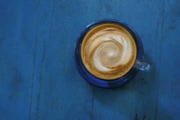 Top view of hot coffee cappuccino cup on blue painted wood table background.