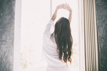 Naklejka premium Asian woman waking up in her bed fully rested and open the curtains in the morning to get fresh air.
