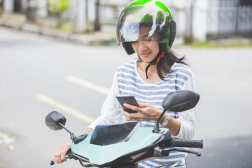 Naklejka premium woman sitting on her motorbike and using mobile phone