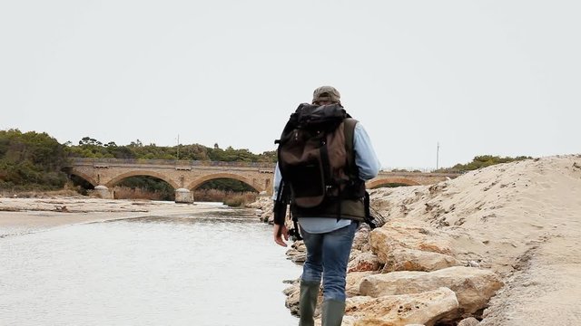 An explorer walking towards a bridge near a river.
