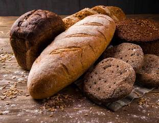 A variety of fresh bread lay on a wooden table. Pastries made from wheat and rye flour