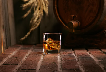 Glass of whiskey and wooden barrel in cozy cellar - obrazy, fototapety, plakaty