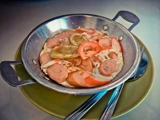 Fried eggs in pan on dish with hot-dog, tomato, vegetable and sauce on table