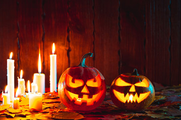 Halloween pumpkin with glowing face on a wooden background with candles