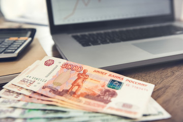 Russian Ruble money banknotes on a wooden desk with a laptop and a calculator