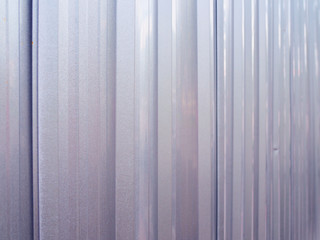 Shiny grey new steel wavy fence wall background for protecting construction site, perspective close up shot, selective focus