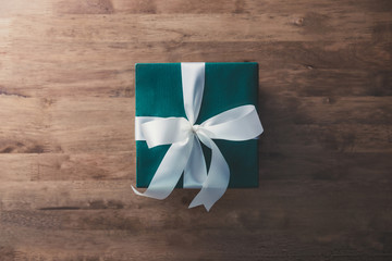 Christmas and New Year holidays gift box wrapped with green paper and white ribbon bow on wood table