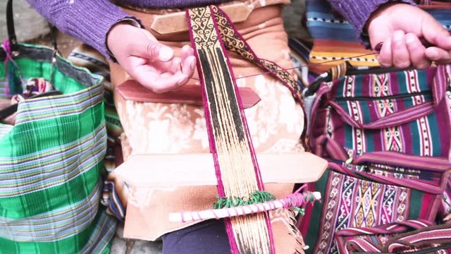 Indigenous woman weaves yarn a foot loom at downtown Cusco, Peru. Slow motion	Woman with her handcraft