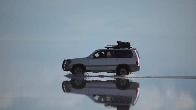 Off-road car on reflected surface of dry salt lake Salar de Uyuni in Bolivia. Slow motion
