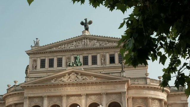 Static close shot of the upper floors of Alte Oper, the opera theatre in Frankfurt taken from Opernplatz and framed by trees