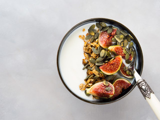 Healthy breakfast natural yogurt bowl with home made granola, pumpkin seeds and figs on gray background