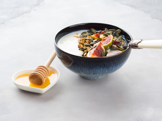 Healthy breakfast natural yogurt bowl with home made granola, pumpkin seeds and figs on gray background