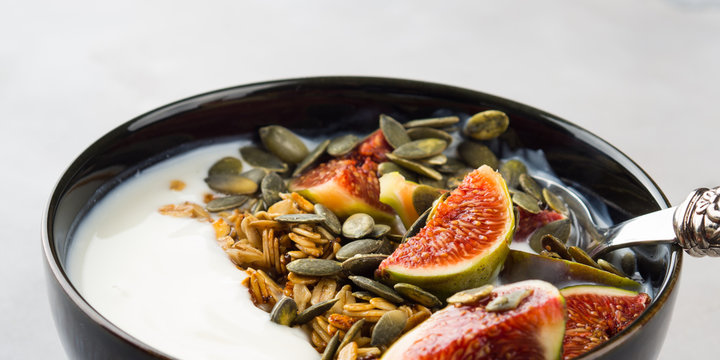 Healthy breakfast natural yogurt bowl with home made granola, pumpkin seeds and figs on gray background